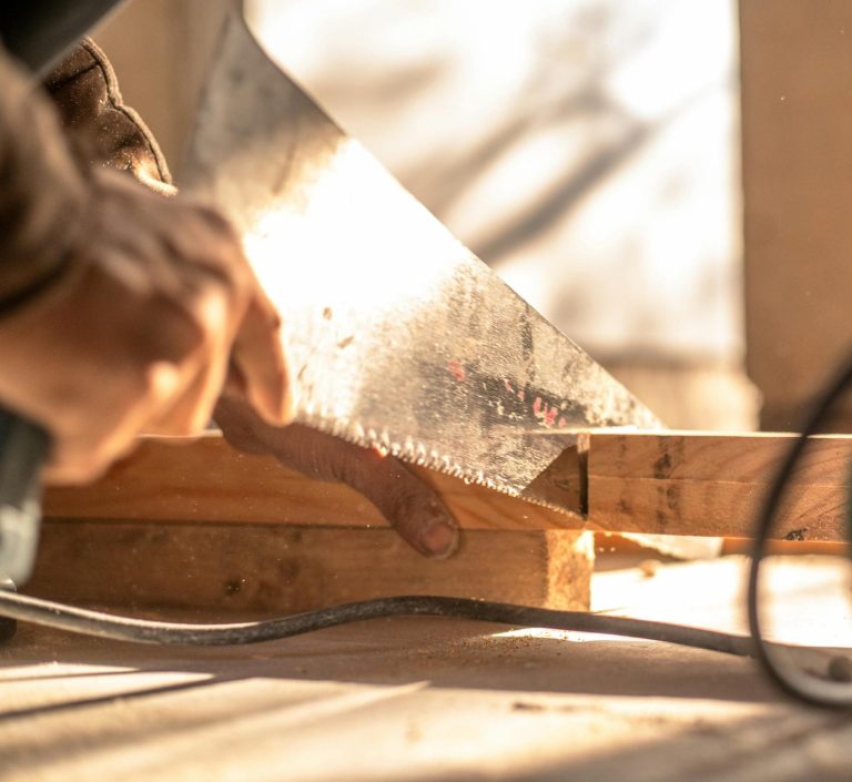 Handwerker Holzbau Ein Handwerker sägt ein Holzstück mit einer Handsäge in einem hellen Raum.